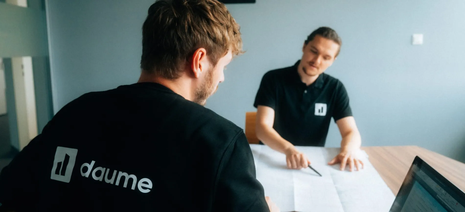 Zwei Kollegen besprechen gemeinsam Baupläne an einem Tisch im Büro, du kannst Teil des Teams werden.