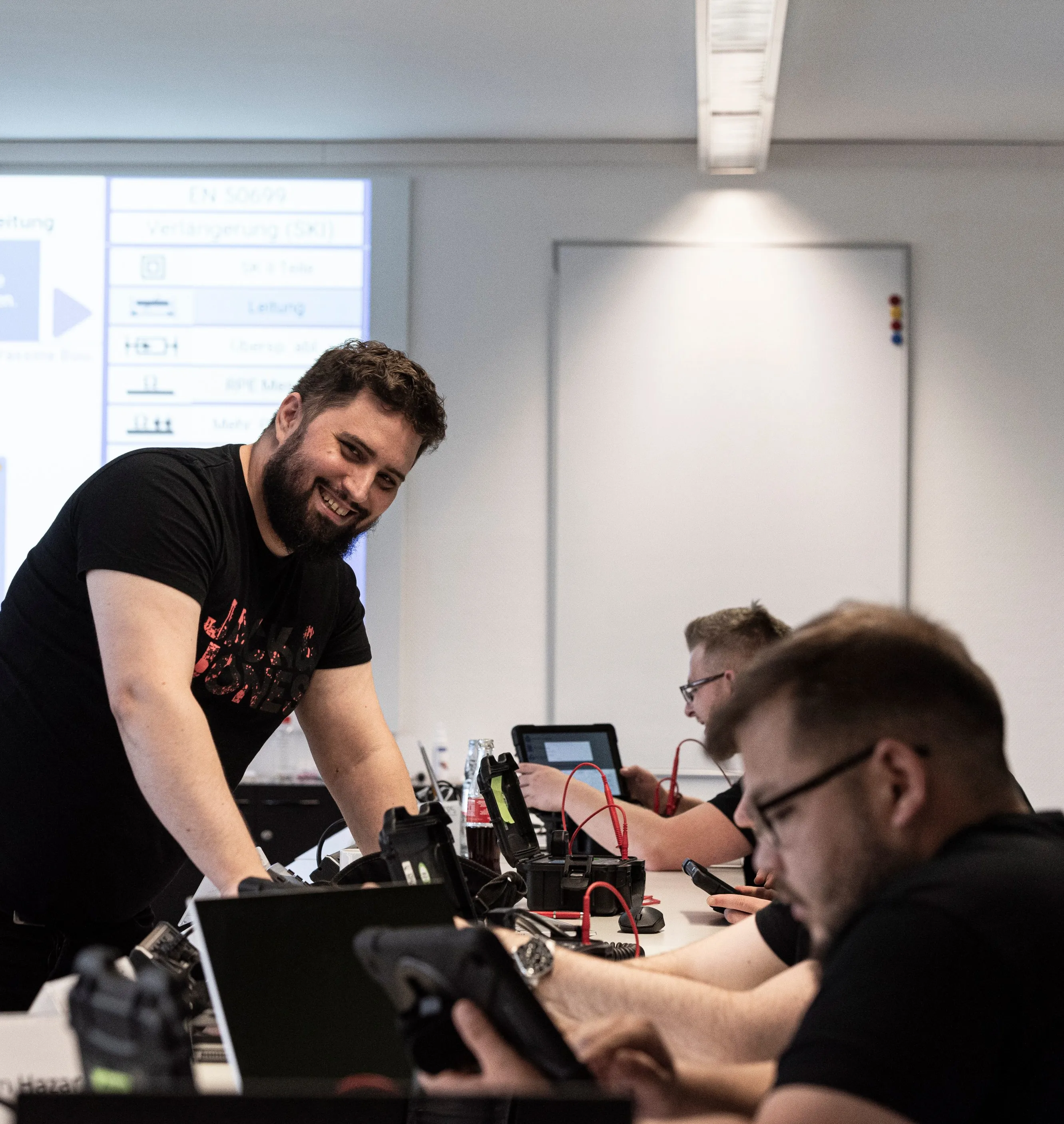 Ein lächelnder Mann erklärt einer Gruppe von Kollegen technische Geräte in einem modernen Büro.