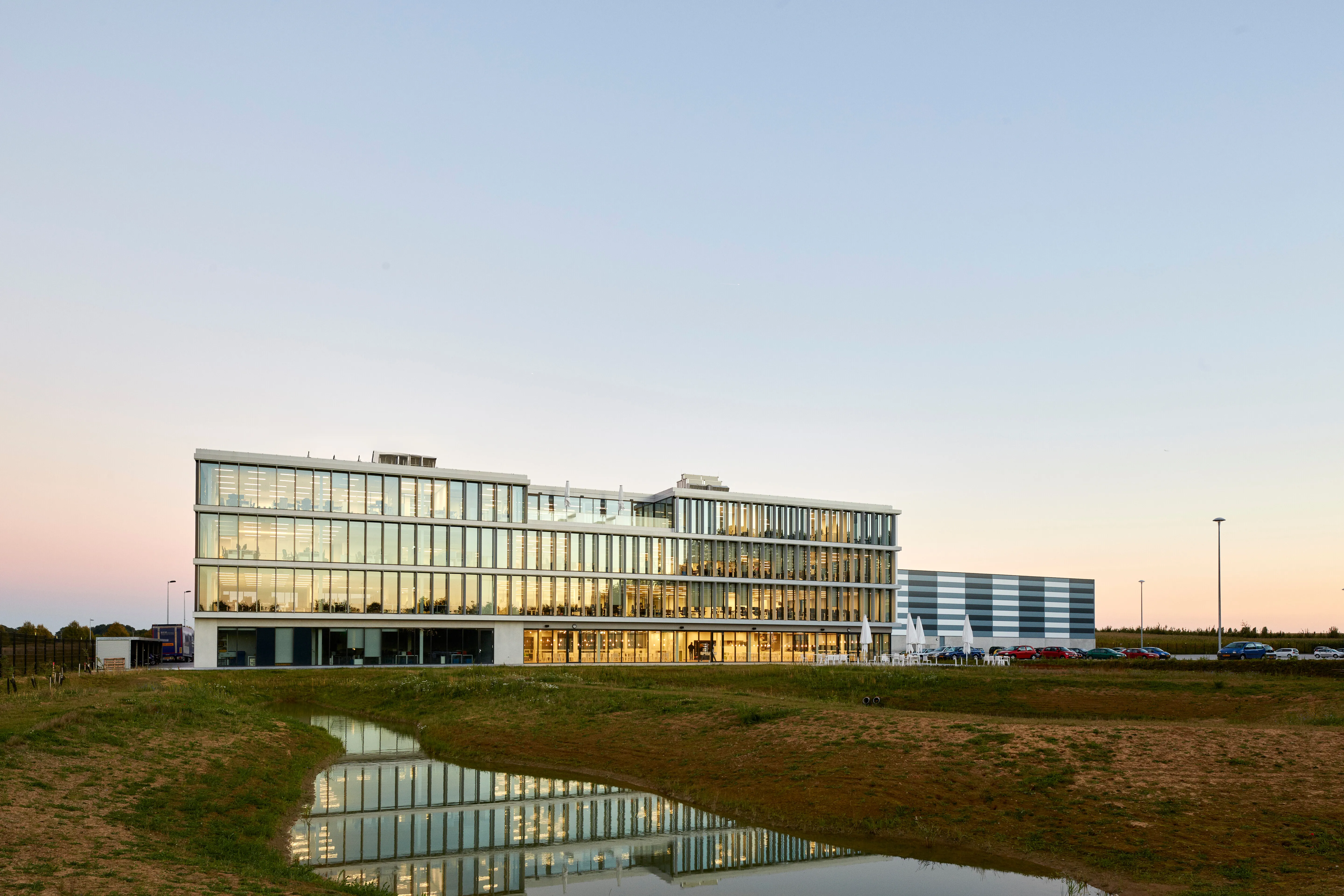 Modern DocMorris office building at sunset, reflecting in a nearby pond, set in a serene landscape.