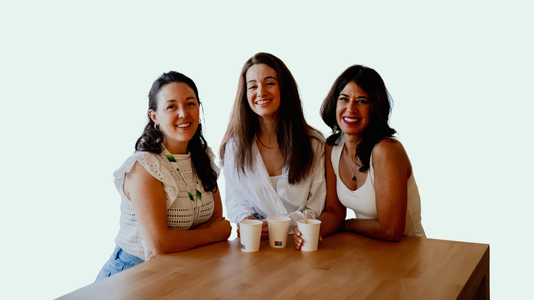 Tres compañeras sonrientes en una mesa de oficina, disfrutando de un café en PromoFarma por DocMorris.