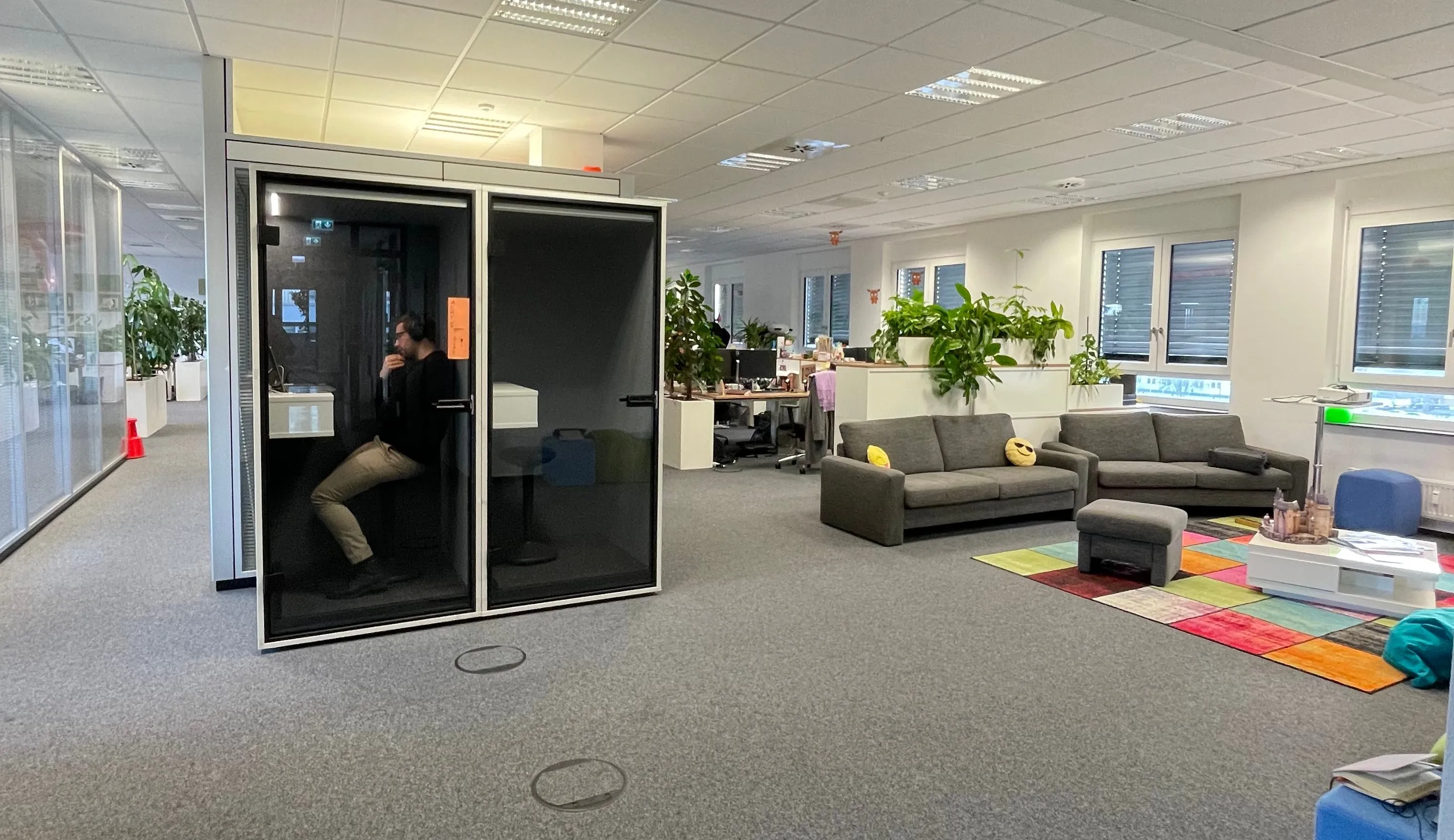 Modern office space at DocMorris with cozy seating, colorful rug, and a soundproof pod for focused work.