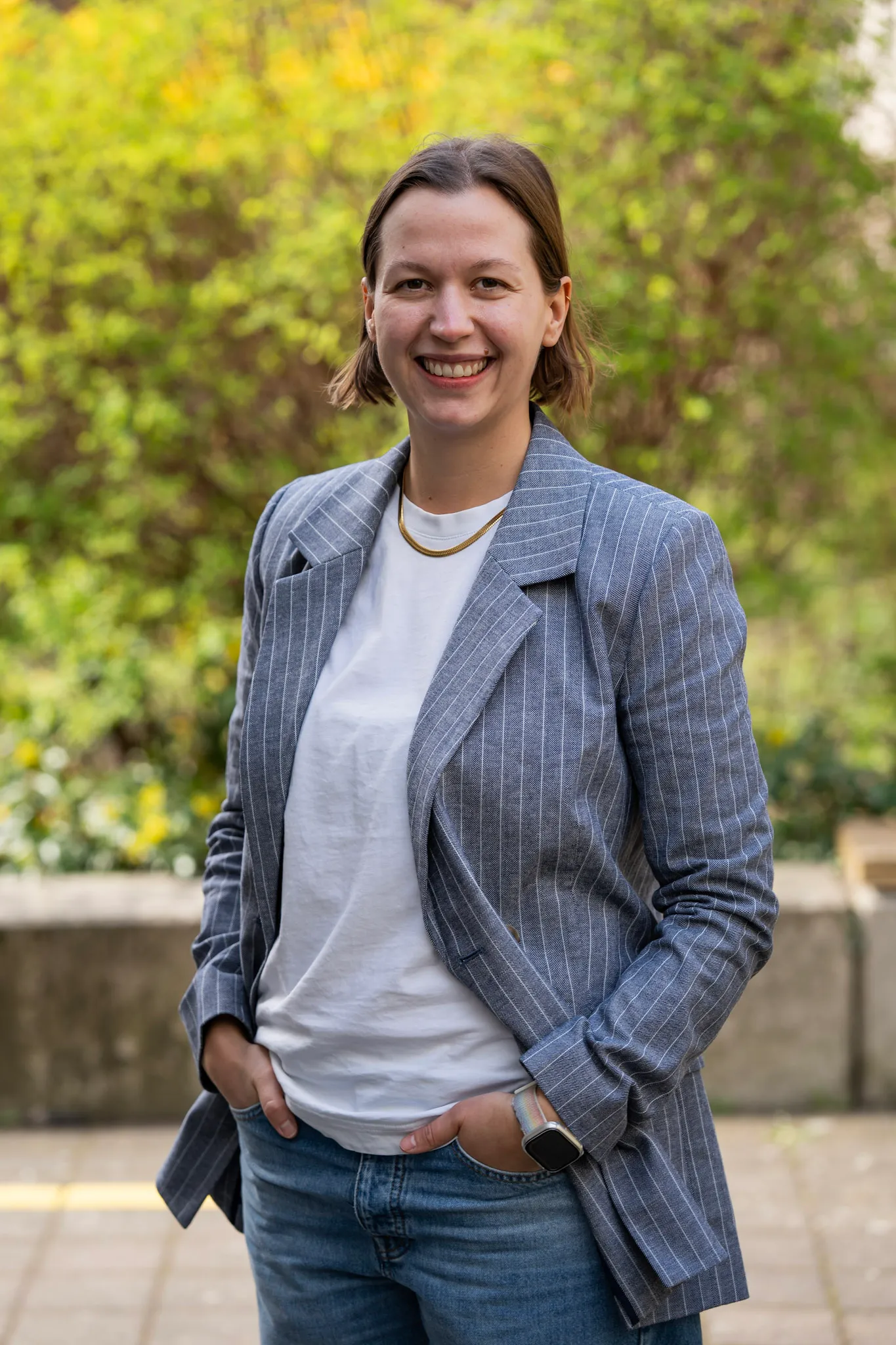 Smiling woman in a pinstripe blazer standing confidently in front of a brick wall, representing DocMorris healthcare careers.