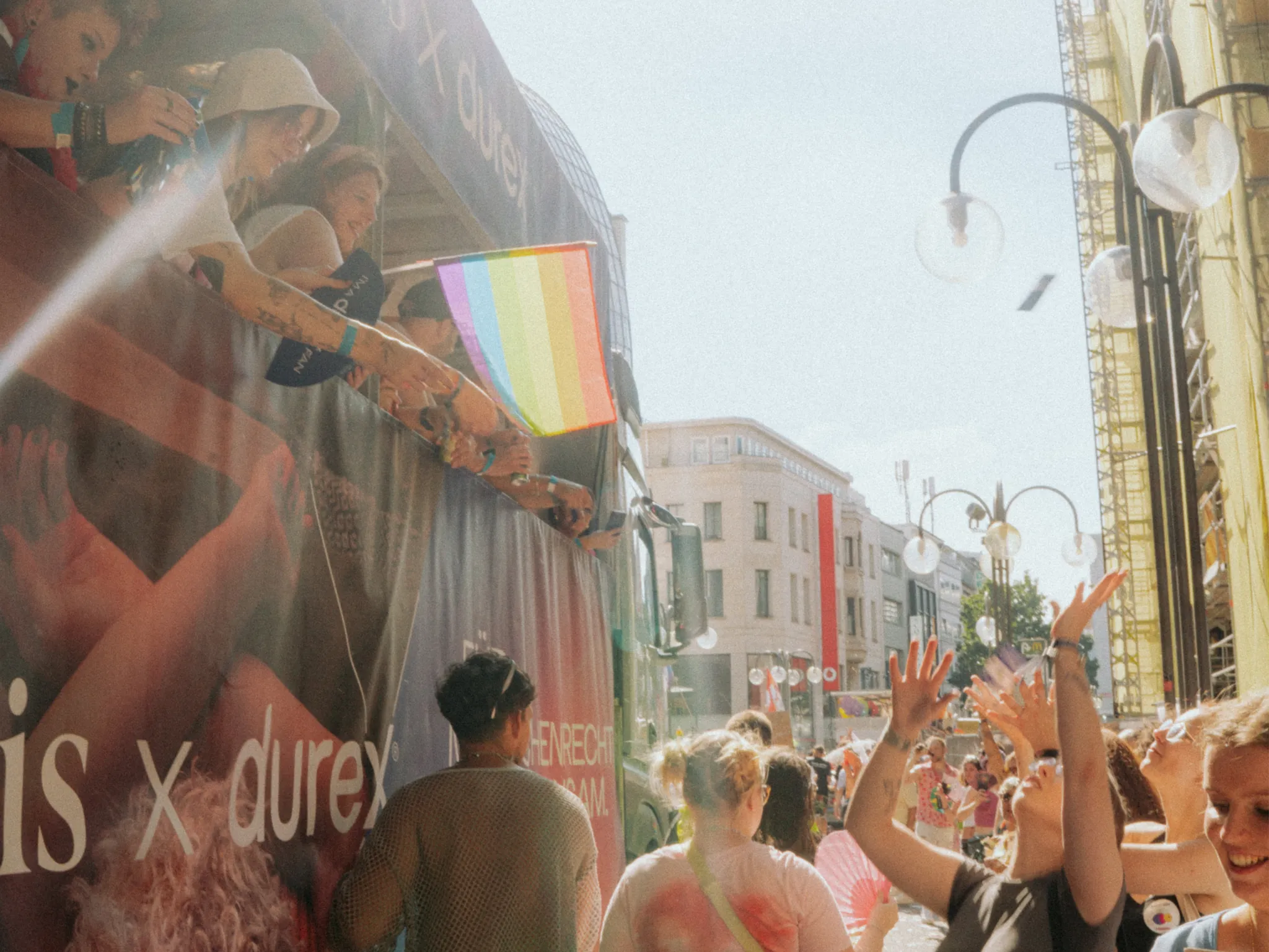 People enjoying a lively street event with a rainbow flag, capturing the vibrant spirit of the day.