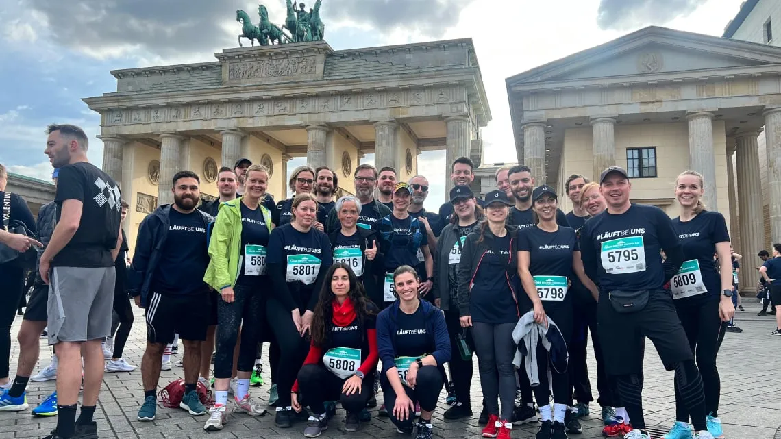 Ein Team der doctari group posiert lächelnd nach einem Lauf-Event vor dem Brandenburger Tor in Berlin.