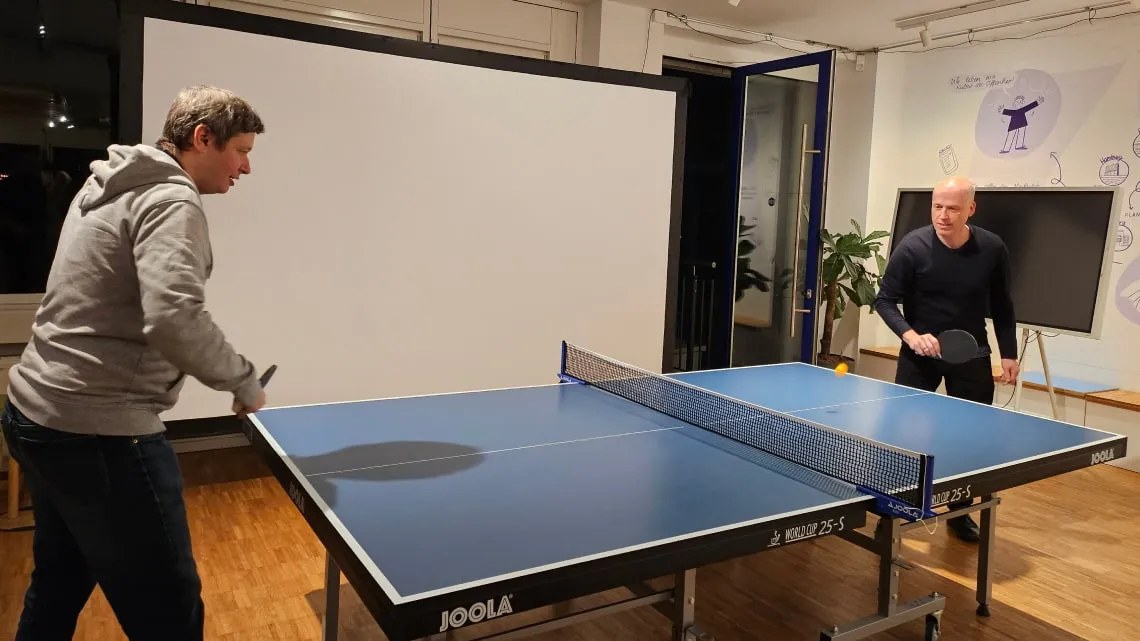 Zwei Kollegen spielen Tischtennis im modernen Büro der doctari group und haben gemeinsam Spaß nach der Arbeit.