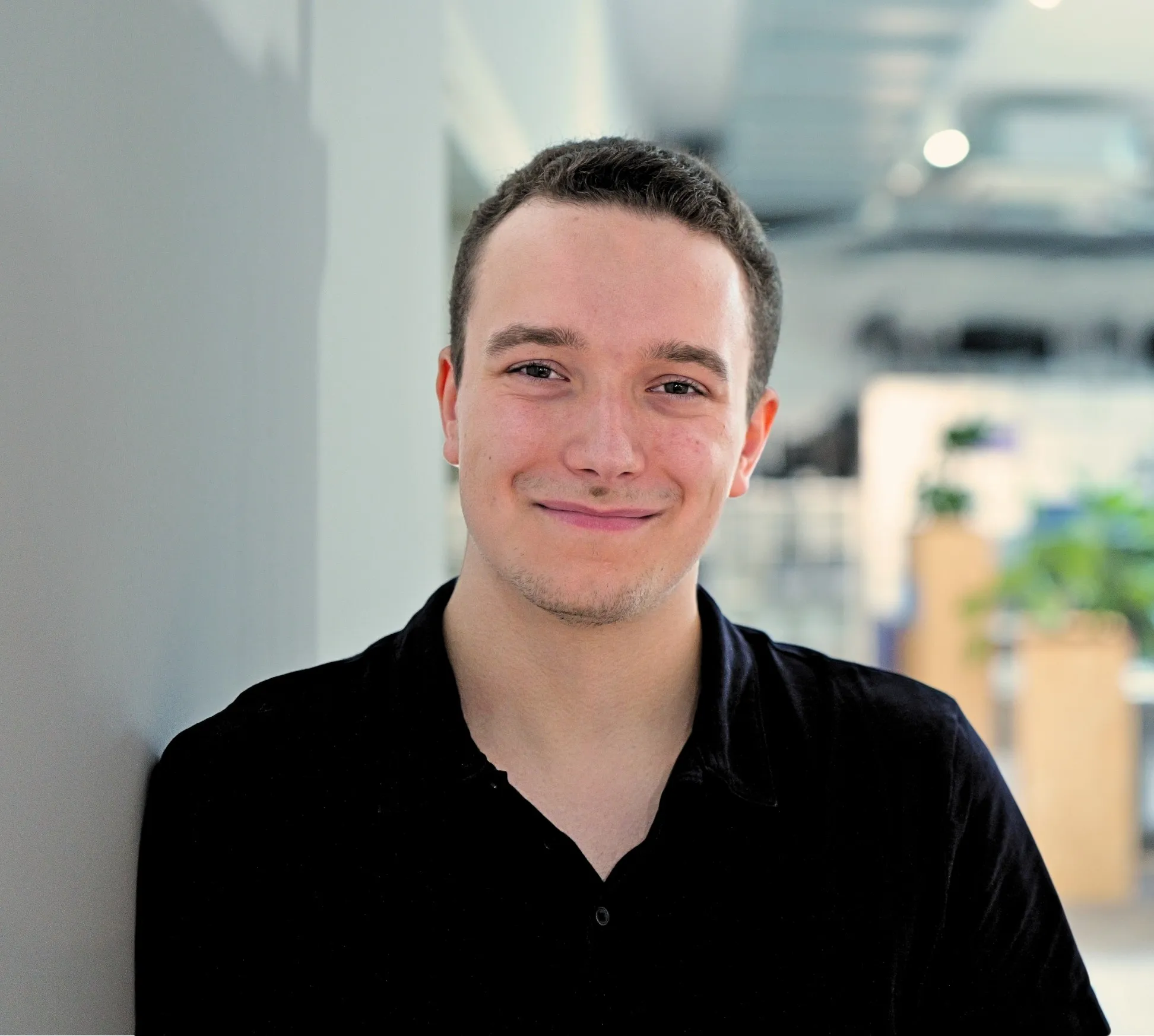 Junger Mann lächelt entspannt in die Kamera, im modernen Büro der Medien- und Entertainmentbranche.