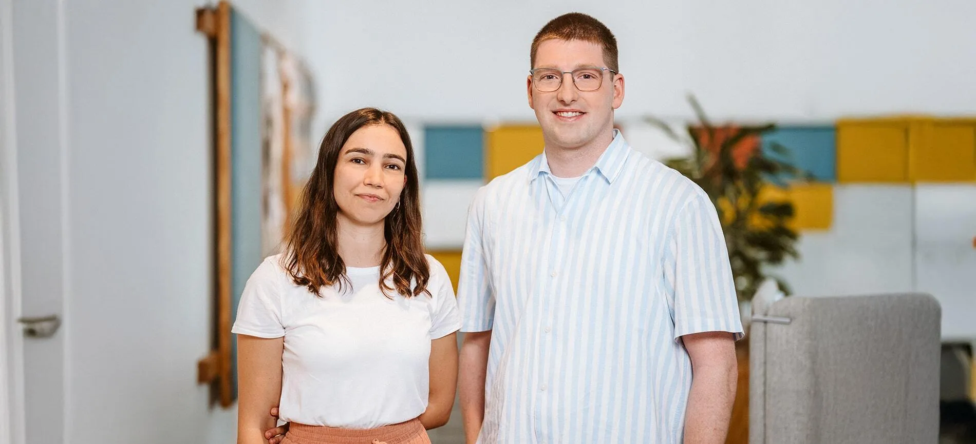Zwei junge Mitarbeitende von doctari group lächeln gemeinsam in einem modernen Büro der Medien- und Entertainmentbranche.
