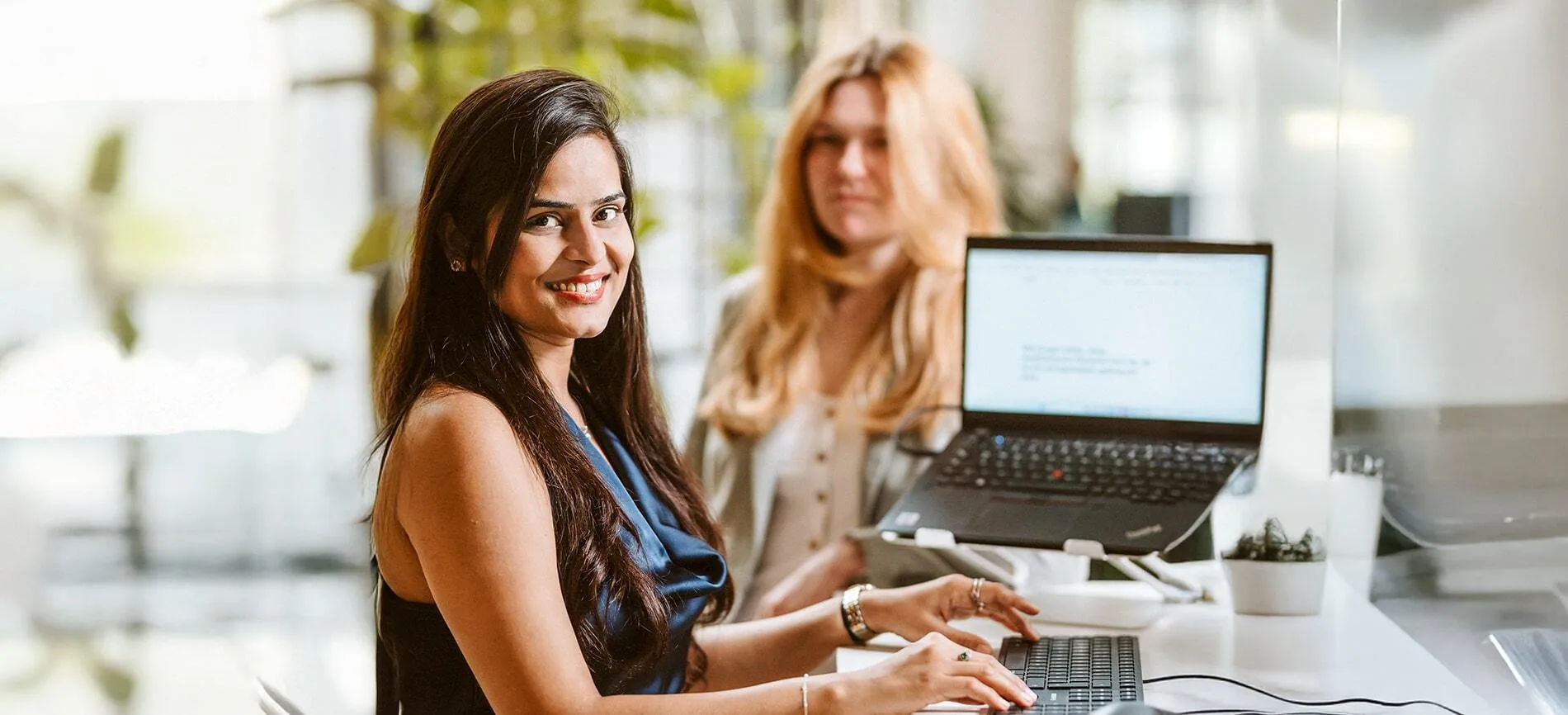 Zwei junge Frauen arbeiten gemeinsam am Schreibtisch, Du wirst herzlich zur Teamarbeit bei doctari group eingeladen.