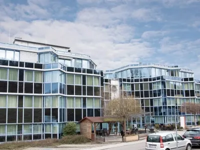 Moderne Gebäude des Pflegeheims Seniorenresidenz Leonberg von Domus Cura GmbH mit Glasfassade und Parkplatz im Vordergrund.