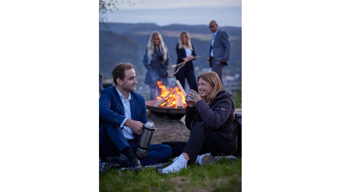 Junge Kollegen von DORNBACH sitzen entspannt am Lagerfeuer in der Natur und genießen gemeinsam eine Pause.