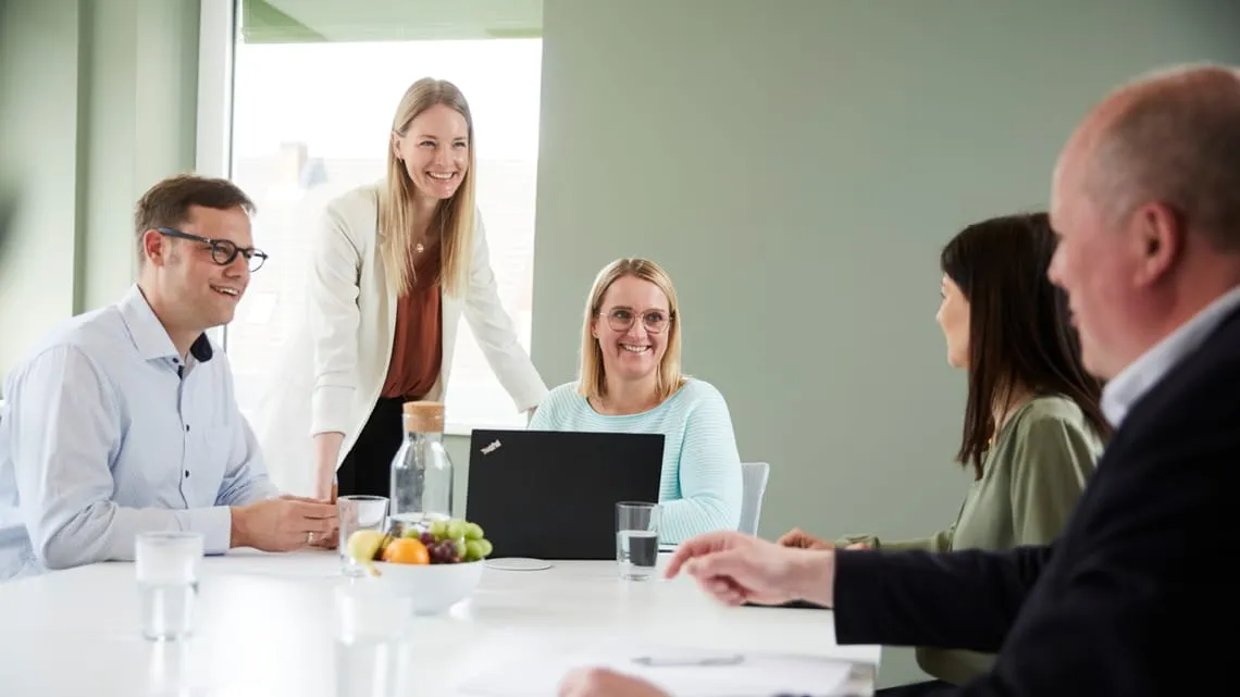 Ein Team aus fünf Kolleg:innen tauscht sich in entspannter Atmosphäre im Besprechungsraum eines Pharmaunternehmens aus.