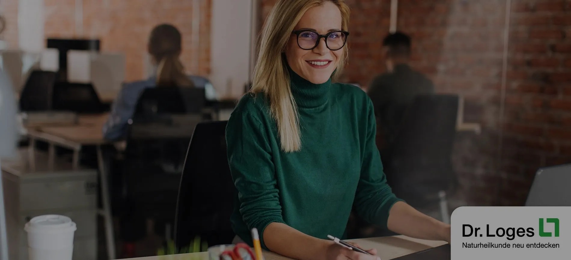 Junge Frau mit Brille lächelt im modernen Büro bei der Arbeit, ideal für Deinen Einstieg in die Pharmabranche.