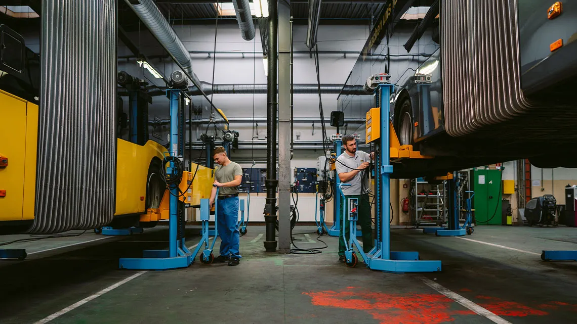 Zwei Mechaniker arbeiten an hochgehobenen Gelenkbussen in einer modernen Werkstatt.