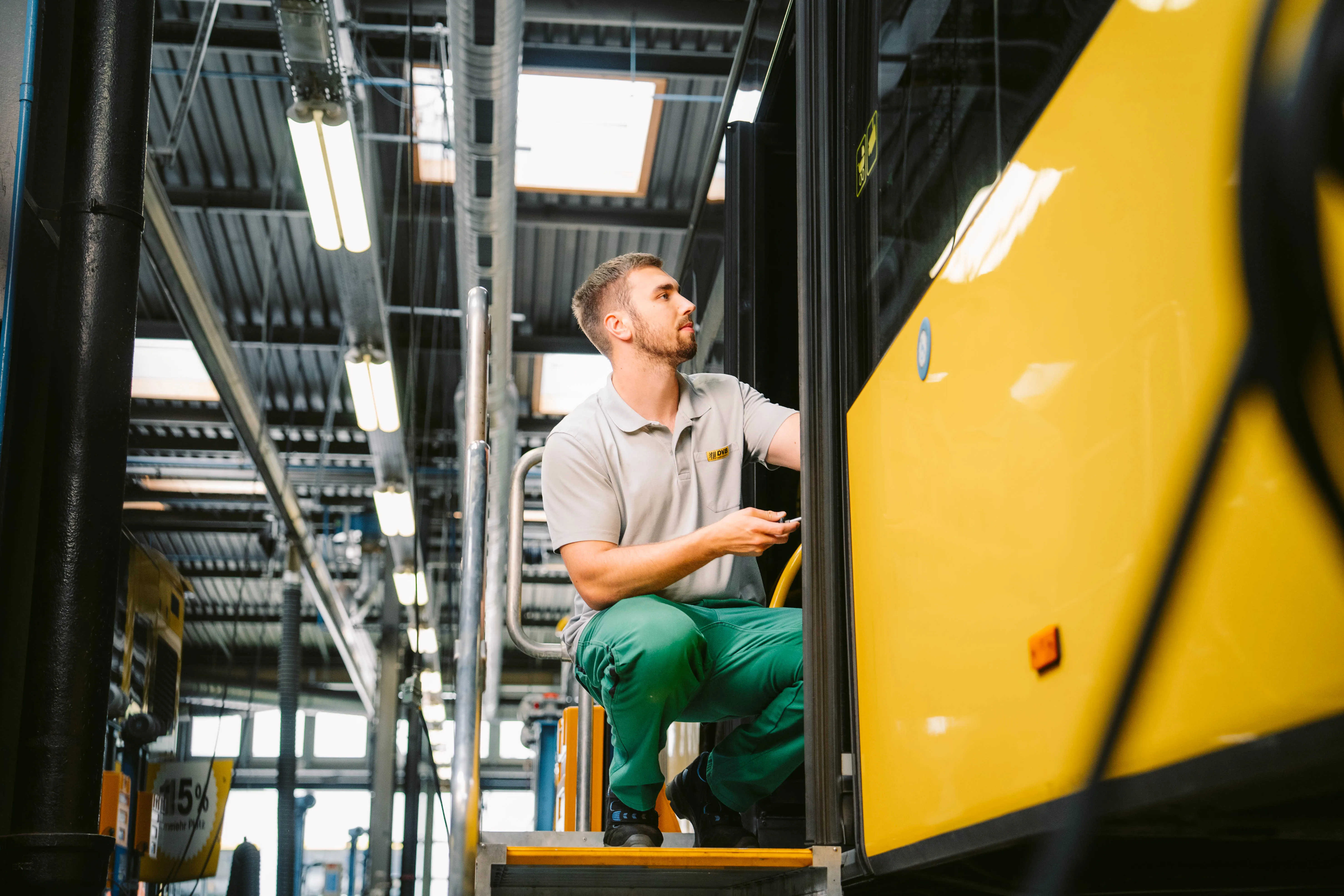 Drei Kollegen besprechen sich in einer Werkstatt zwischen angehobenen Bussen – Teamarbeit im technischen Bereich.