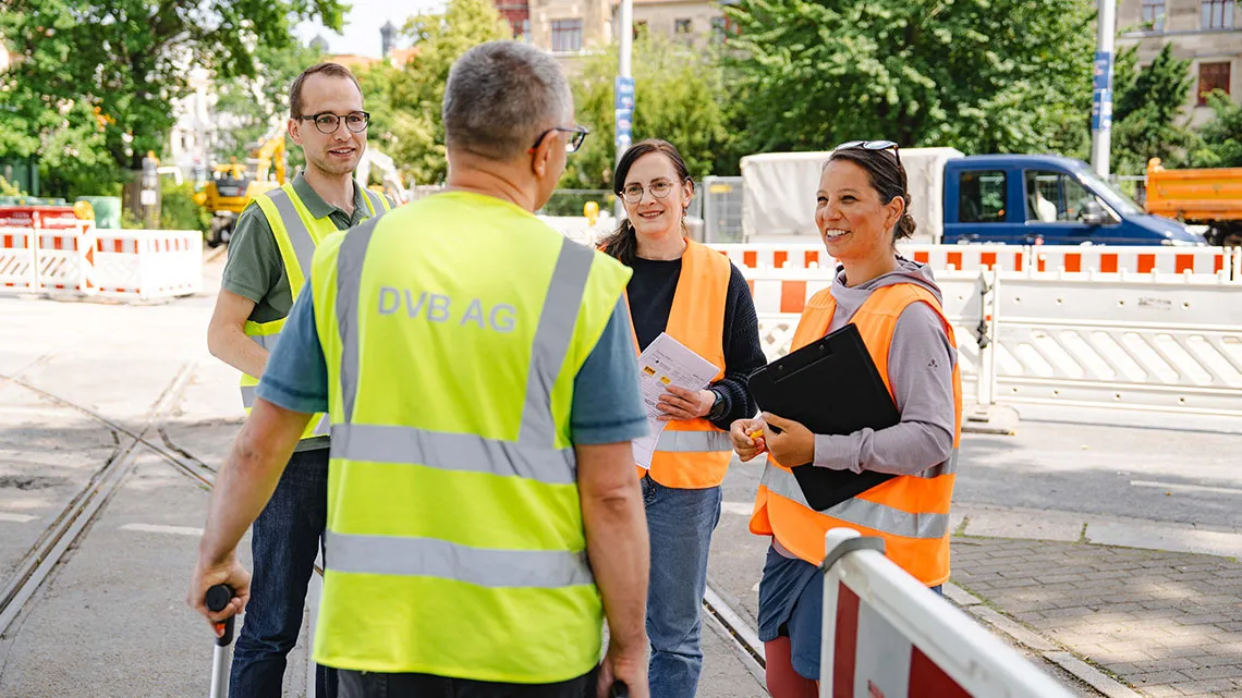 Vier Menschen mit Warnwesten besprechen auf einer Baustelle gemeinsam die nächsten Schritte.