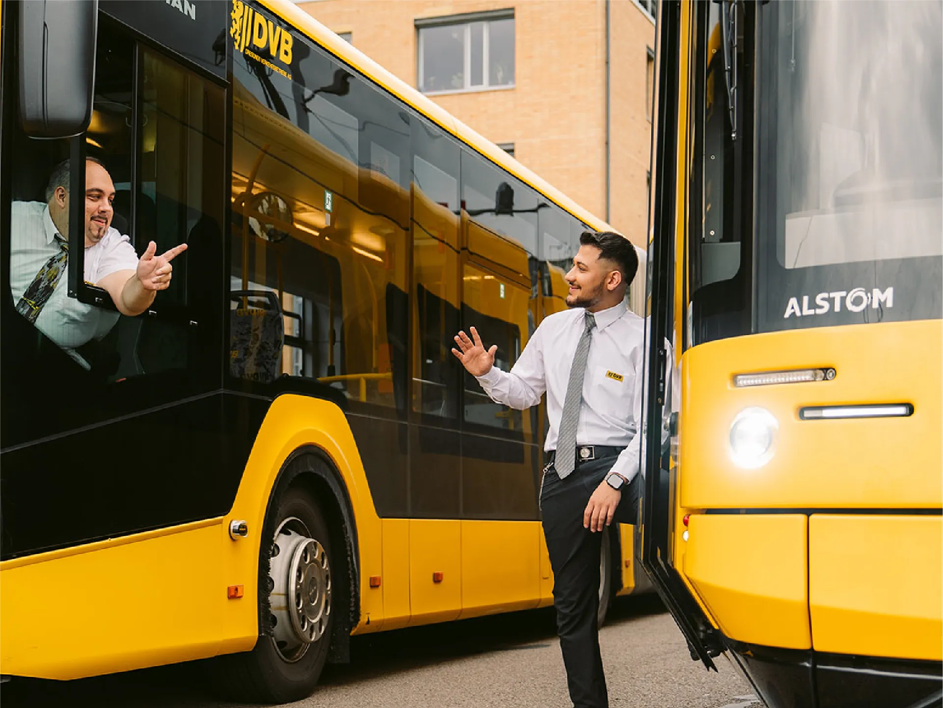 Zwei Busfahrer scherzen miteinander, während einer aus dem Fenster lehnt und der andere an der Tür steht.