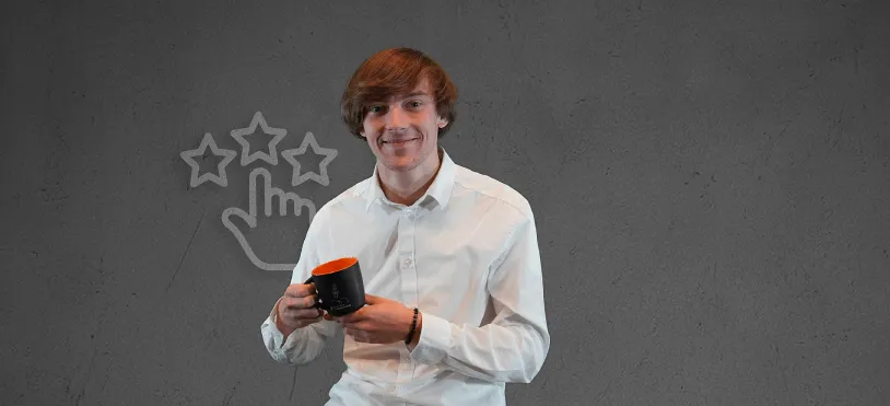 Junger Mann im weißen Hemd hält eine Tasse und lächelt vor einer Wand mit gezeichneten Sternen und Hand-Symbol.