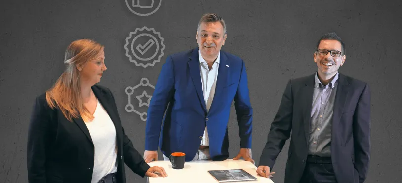 Drei Kolleg:innen von E/D/E stehen lächelnd an einem Tisch und wirken offen und einladend für neue Teammitglieder.