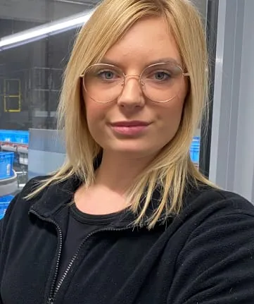 Junge Frau mit Brille und schwarzer Jacke steht im Lagerbereich von EDEKA Nordwest und schaut freundlich in die Kamera.