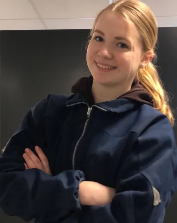 Junge Mitarbeiterin im EDEKA Arbeitsoutfit lächelt freundlich mit verschränkten Armen in die Kamera.