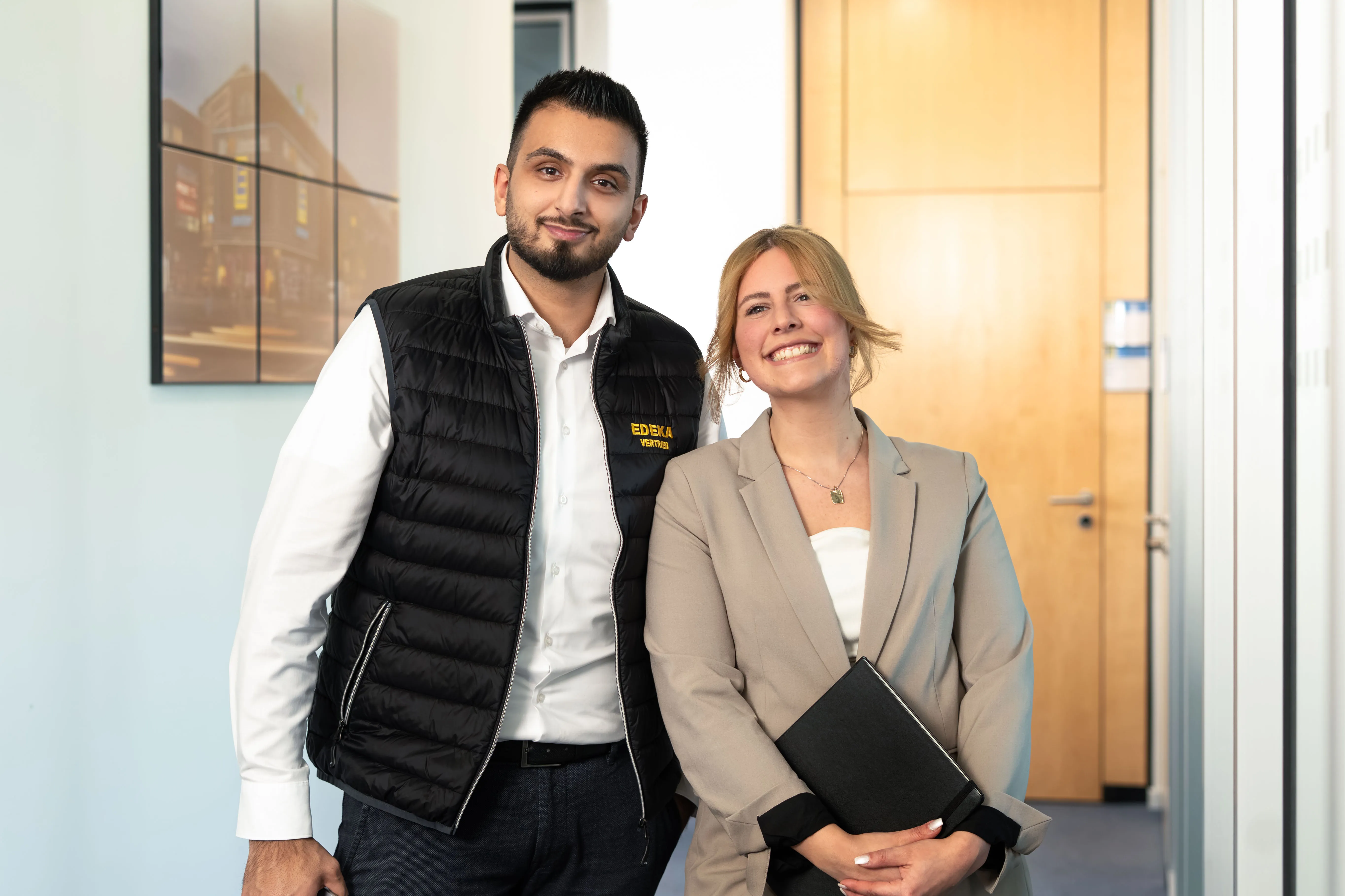 Ein Mann steht in einem Büroflur von EDEKA Nord, hält einen Laptop und blickt lächelnd zur Seite.