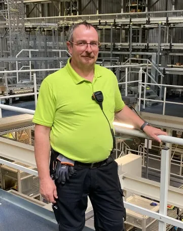 Ein Mitarbeiter im gelben Polohemd steht mit Funkgerät in einer modernen Lagerhalle von EDEKA Nordwest.
