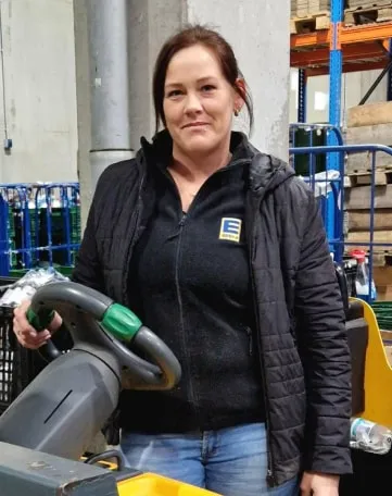 Mitarbeiterin von EDEKA Nordwest steht an einem Gabelstapler im Lager und lächelt in die Kamera.