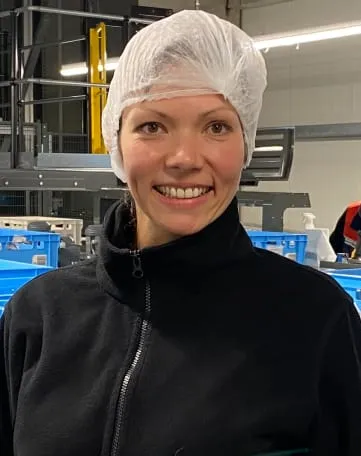 Junge Frau mit Haarnetz lächelt in einer Lagerhalle bei EDEKA Nordwest – starte Deine Karriere im Einzelhandel.