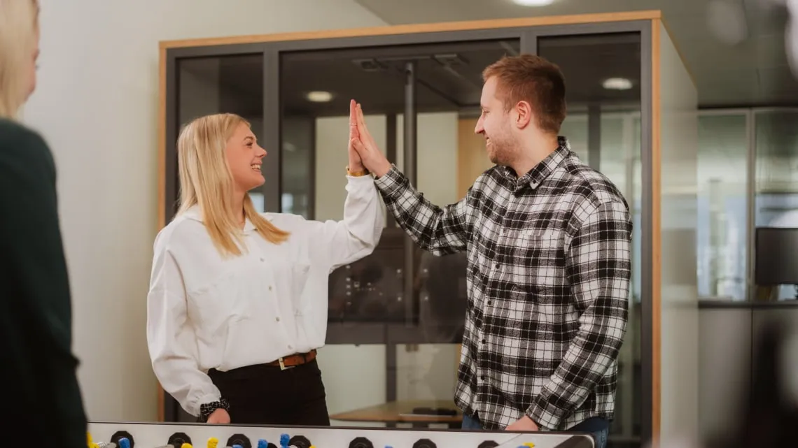 Zwei junge Kollegen geben sich ein High-Five am Kickertisch im modernen EDEKA Nordwest Büro.
