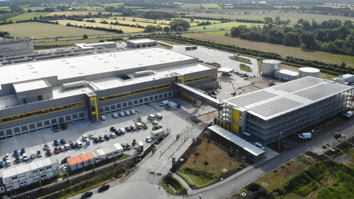 Luftaufnahme des modernen EDEKA Nordwest Logistikzentrums mit Lager, Parkhaus und umgebender Landschaft.