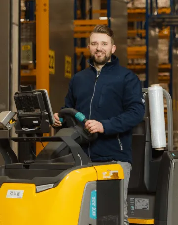 Ein Mitarbeiter von EDEKA Nordwest bedient einen modernen Gabelstapler im Lager und lächelt in die Kamera.