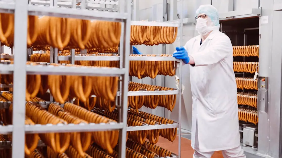 Du siehst eine Person in Schutzkleidung, die Wurstwaren in einer Produktionshalle von EDEKA Nordwest kontrolliert.