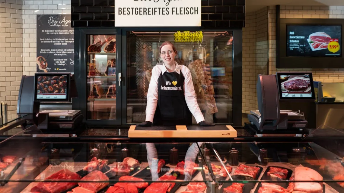 Freundliche Mitarbeiterin an der Frischetheke präsentiert Dir hochwertiges Fleisch im EDEKA Nordwest Markt.