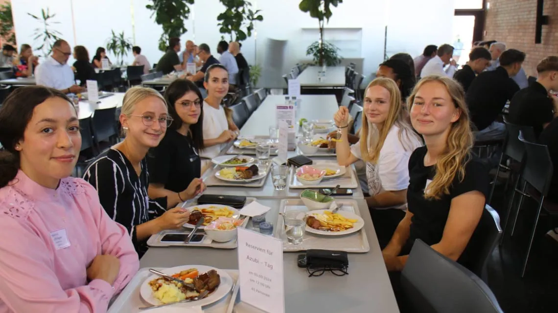 Sechs junge Menschen sitzen gemeinsam in der Evonik-Kantine und genießen ihr Mittagessen am Azubi-Tag.