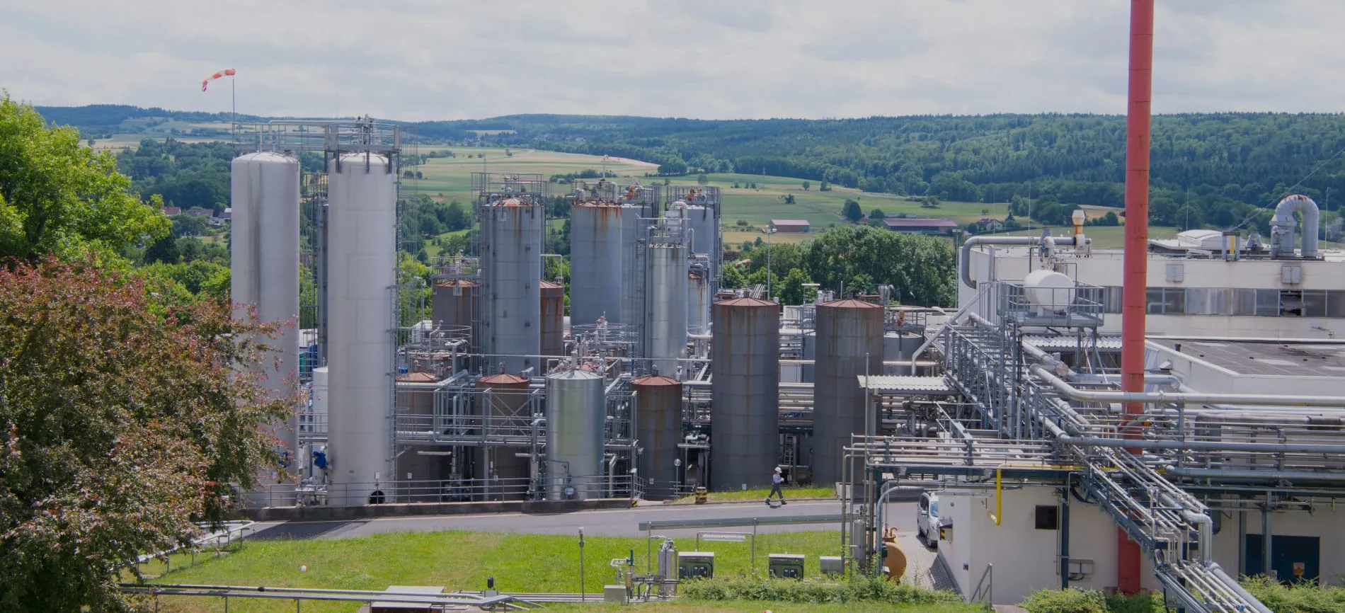 Industrielle Anlage von Evonik mit mehreren Silos und Rohrleitungen vor einer grünen Landschaft.