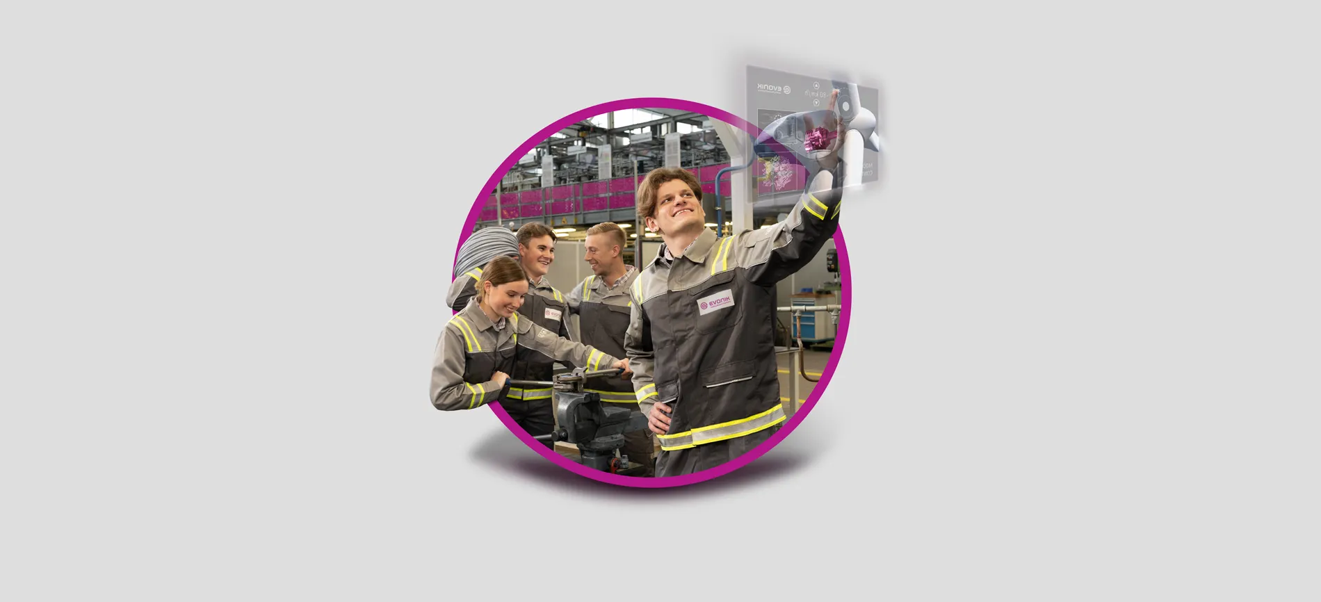 Junge Menschen in Evonik-Arbeitskleidung arbeiten gemeinsam in einer modernen Industriehalle, einer bedient ein digitales Display.