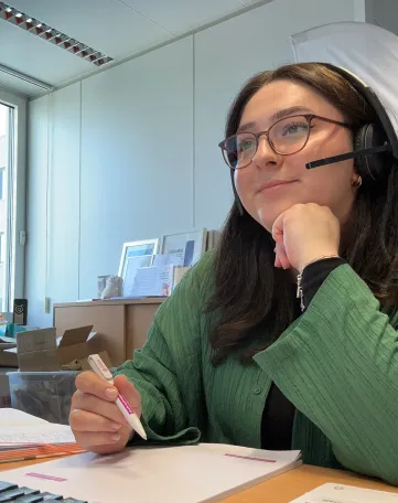 Junge Frau mit Headset arbeitet konzentriert im Büro und macht sich Notizen – deine Karriere bei Evonik im Energiesektor.