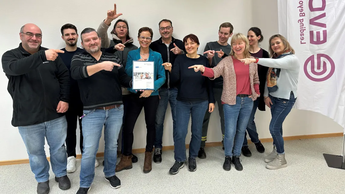 Ein fröhliches Evonik-Team zeigt auf eine Kollegin mit Urkunde – werde Teil unseres Energie- und Versorgungsteams!