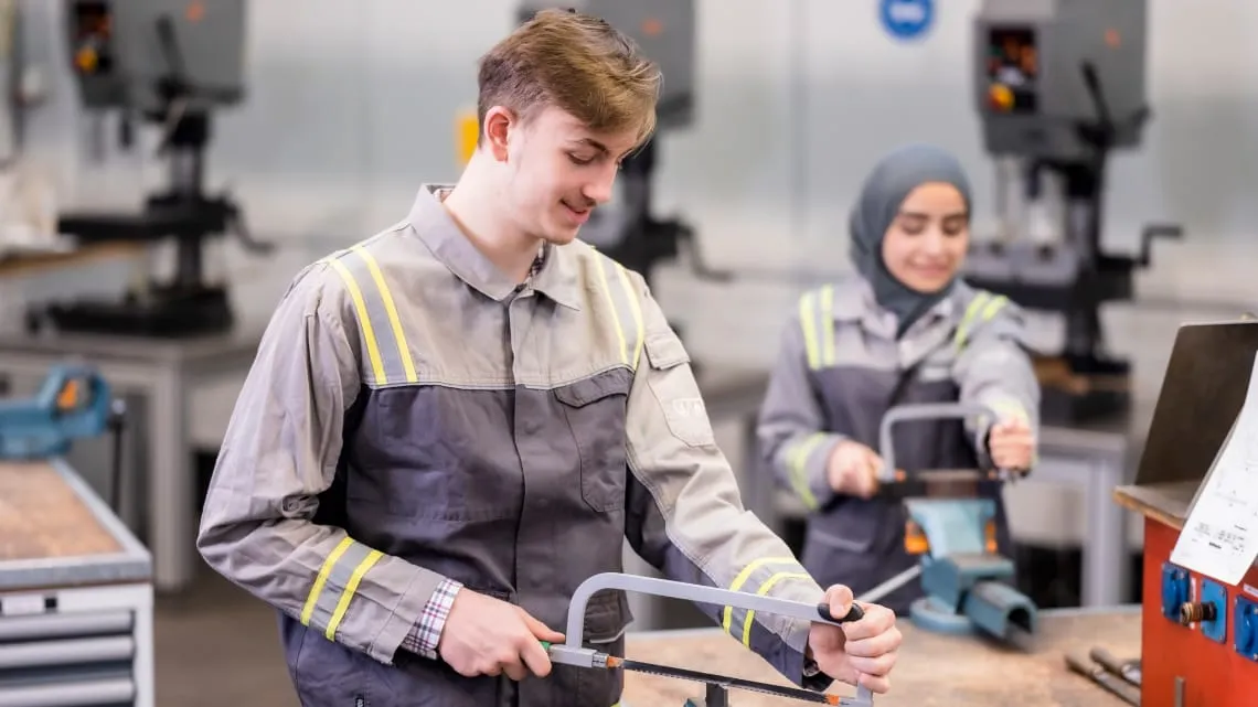 Zwei junge Auszubildende bei Evonik arbeiten gemeinsam im Ausbildungszentrum mit Metallsägen.