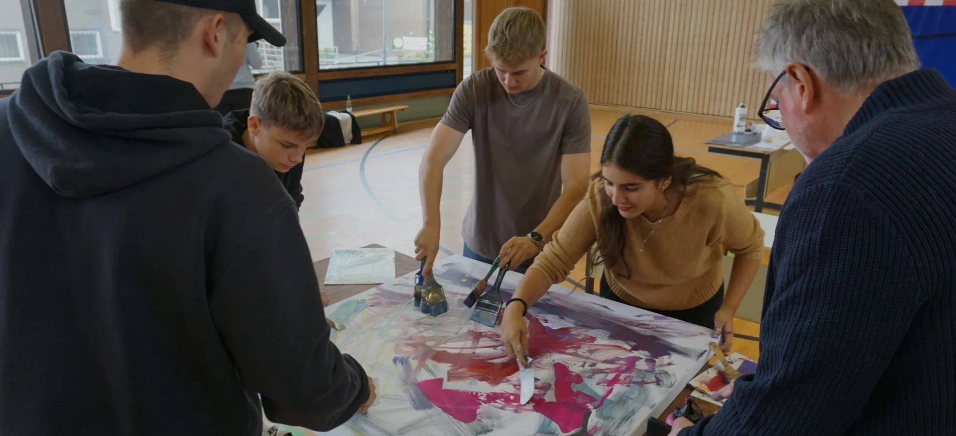 Junge Erwachsene arbeiten gemeinsam an einem Kunstprojekt in einem hellen Raum.