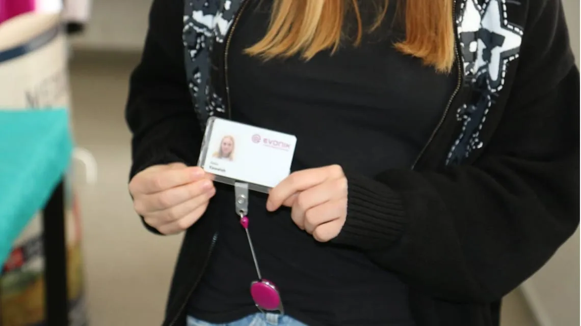 Junge Frau hält Evonik-Mitarbeiterausweis in der Hand – Dein Einstieg in die Energie- und Versorgungsbranche.