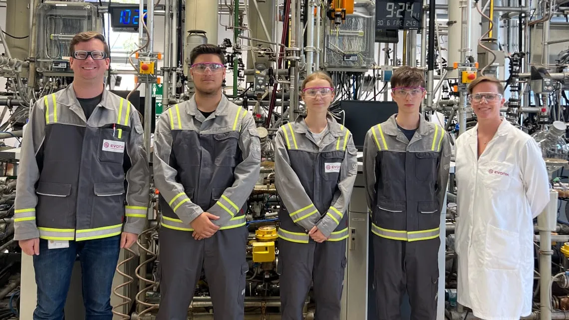 Fünf junge Menschen im Evonik-Werk, tragen Schutzkleidung und stehen vor technischer Anlage in der Energiebranche.