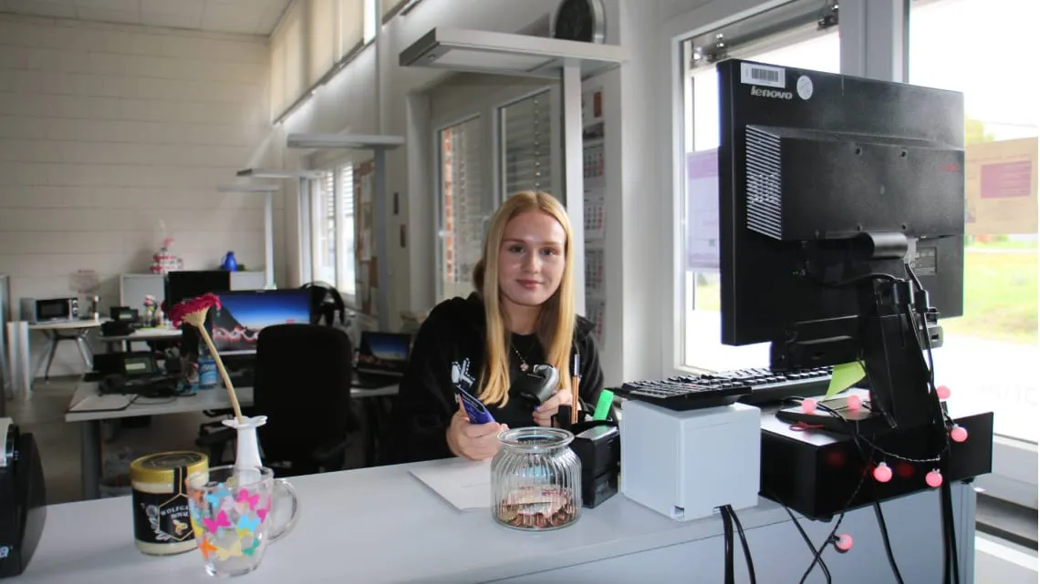 Junge Frau arbeitet am Empfang bei Evonik, begrüßt dich freundlich und nutzt moderne Büroausstattung.