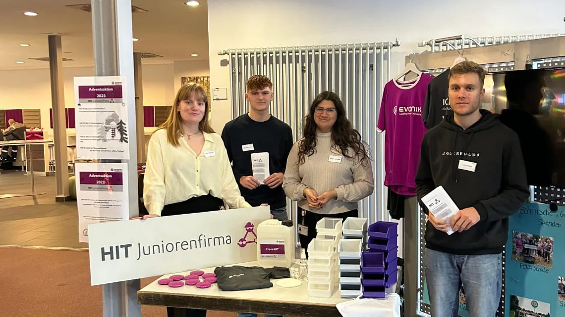 Vier junge Leute am Infostand der HIT Juniorenfirma bei Evonik, präsentieren Projekte und Infos für Deine Karriere.