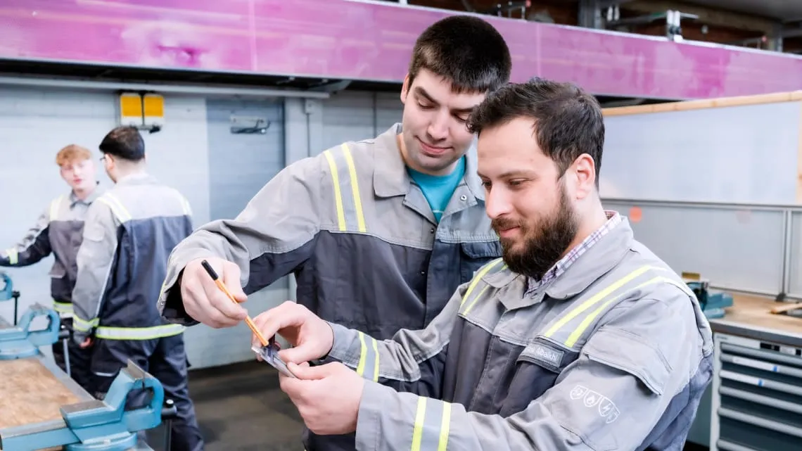 Zwei Auszubildende bei Evonik arbeiten gemeinsam an einem Messwerkzeug in einer Werkstatt.