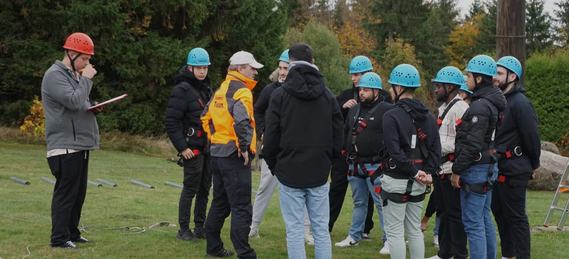 Eine Gruppe von Personen mit Helmen und Sicherheitsausrüstung versammelt sich im Freien, möglicherweise für ein Teambuilding-Event.
