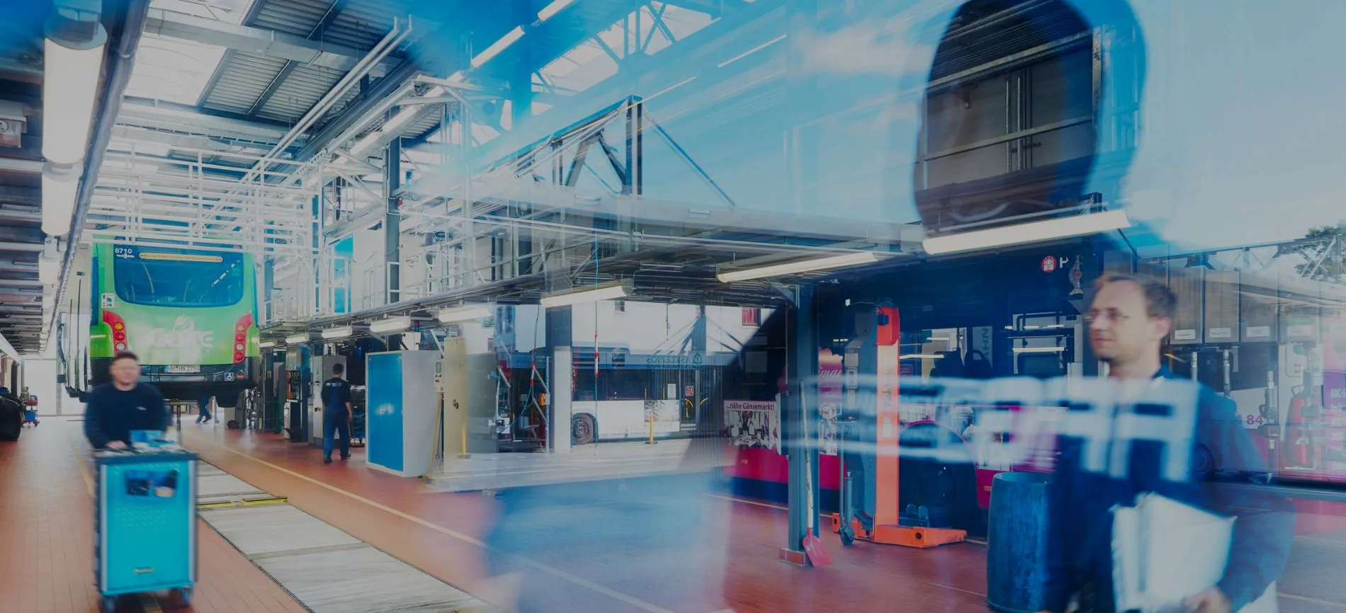 Du siehst eine moderne Werkstatt von FFG mit Bussen und Mitarbeitenden bei der Arbeit im Automotive-Bereich.