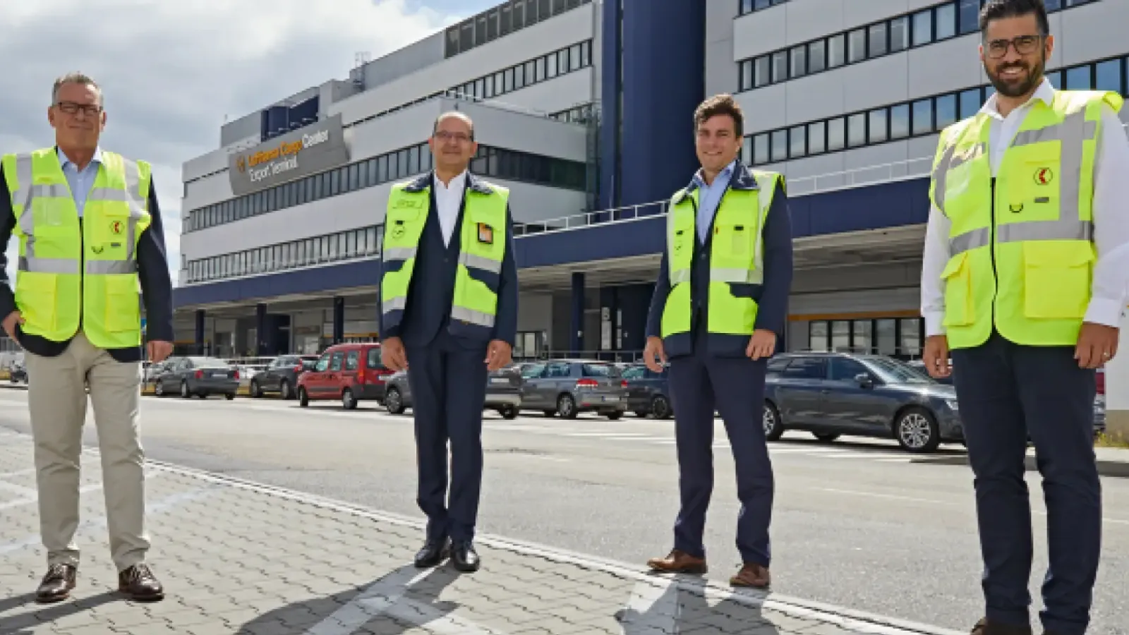 Vier Männer in Warnwesten stehen vor einem Frachtzentrum, das zur Logistikbranche gehört.