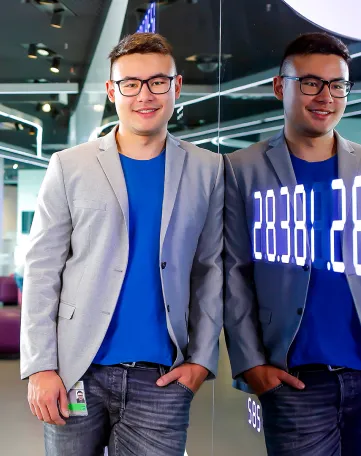 Junger Mann in legerem Business-Outfit steht entspannt vor einer Glaswand im modernen Büro bei Fraport AG.