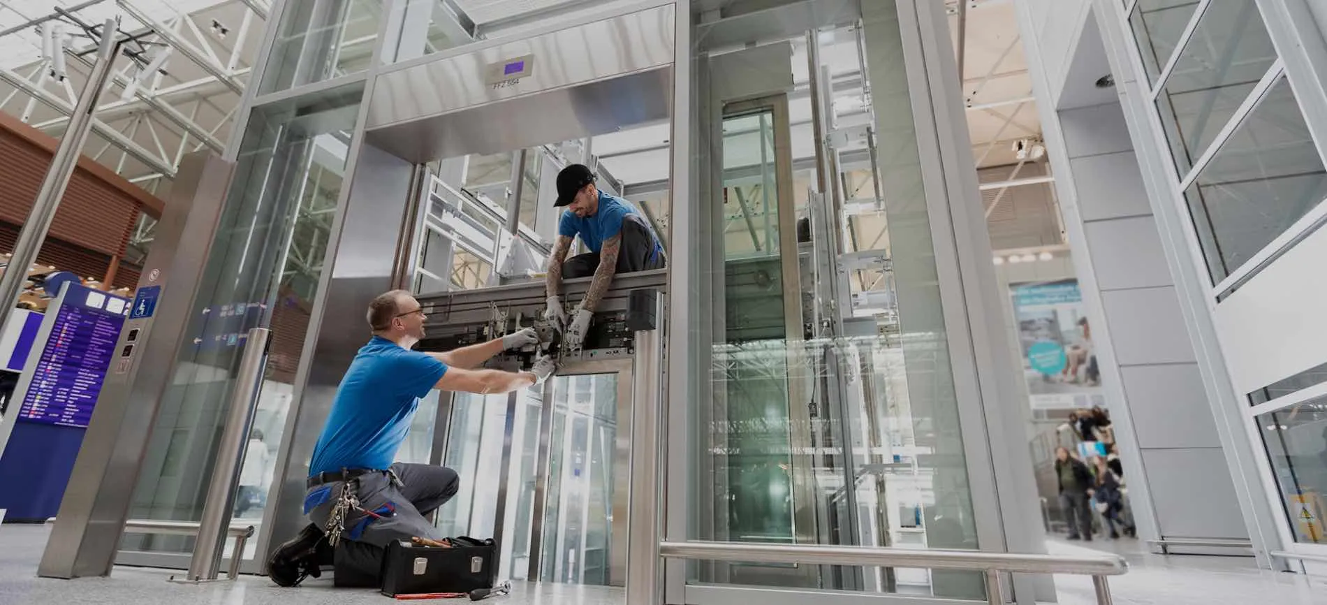 Zwei Techniker warten gemeinsam einen Aufzug im modernen Flughafen, um einen reibungslosen Betrieb zu sichern.